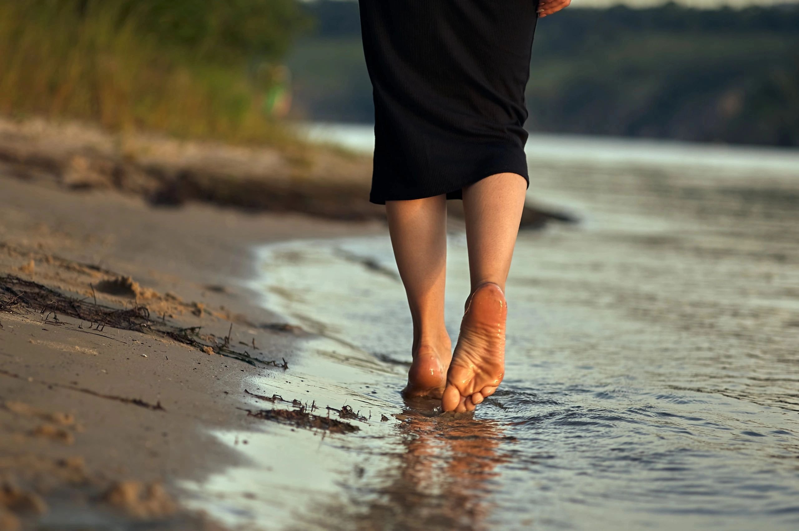 Person walking barefoot on a sandy beach near the water