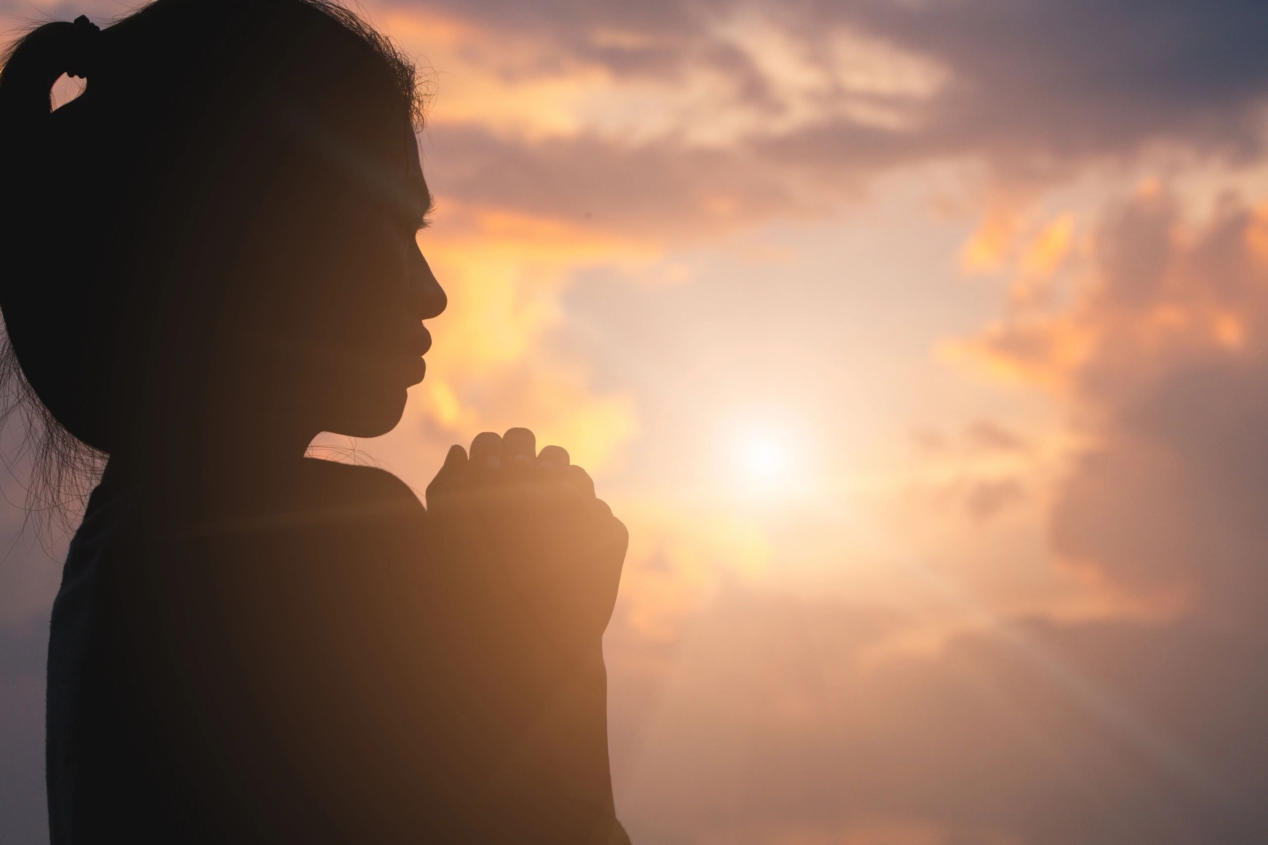 Woman silhouette praying at sunset